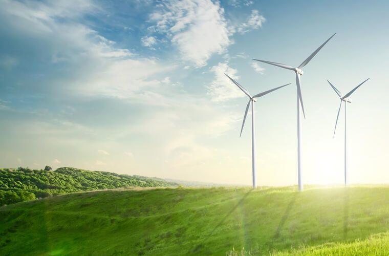 Wind turbines generating electricity across a green landscape under a bright sky